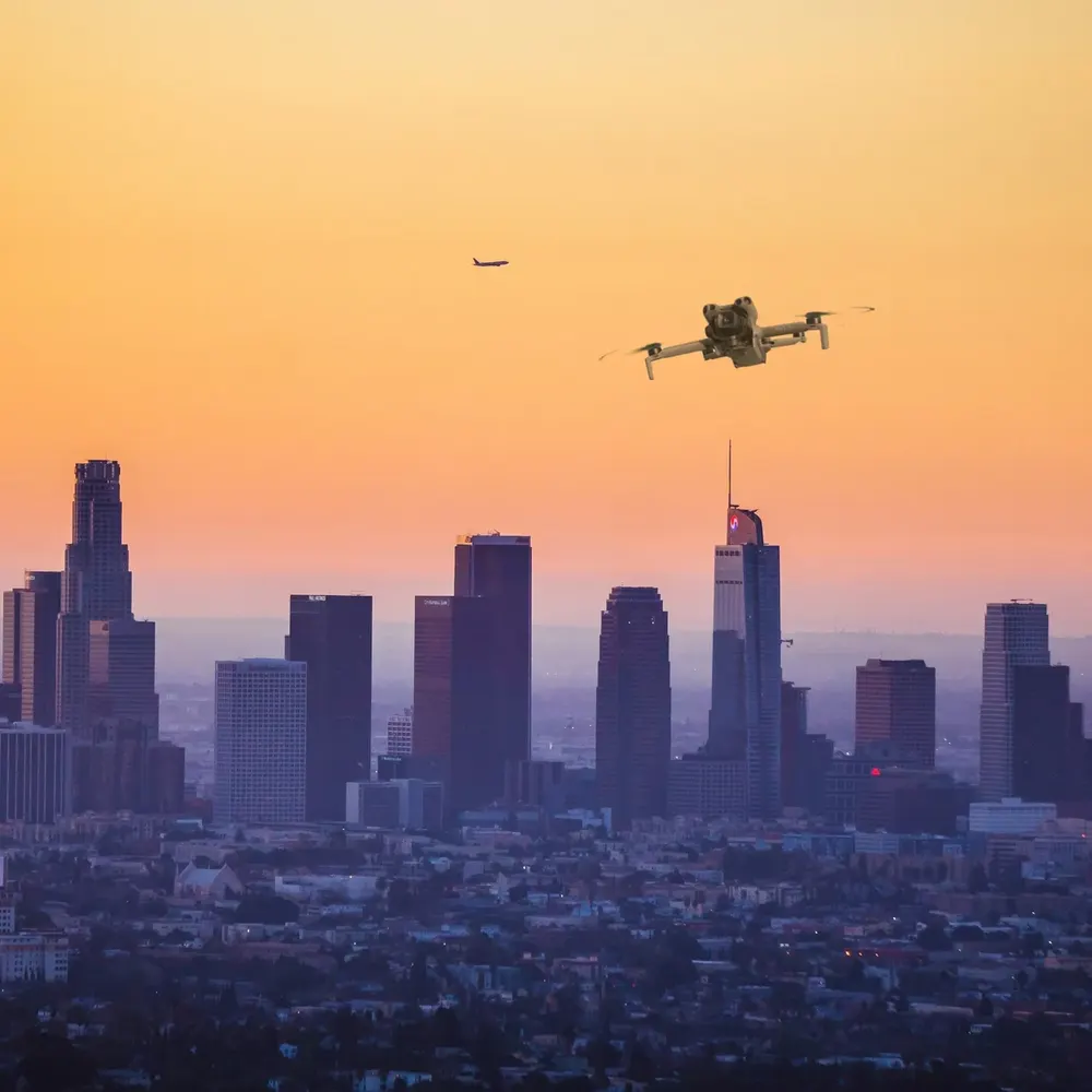 DJI Mini 5 Pro against a city skyline at dusk (composite image)