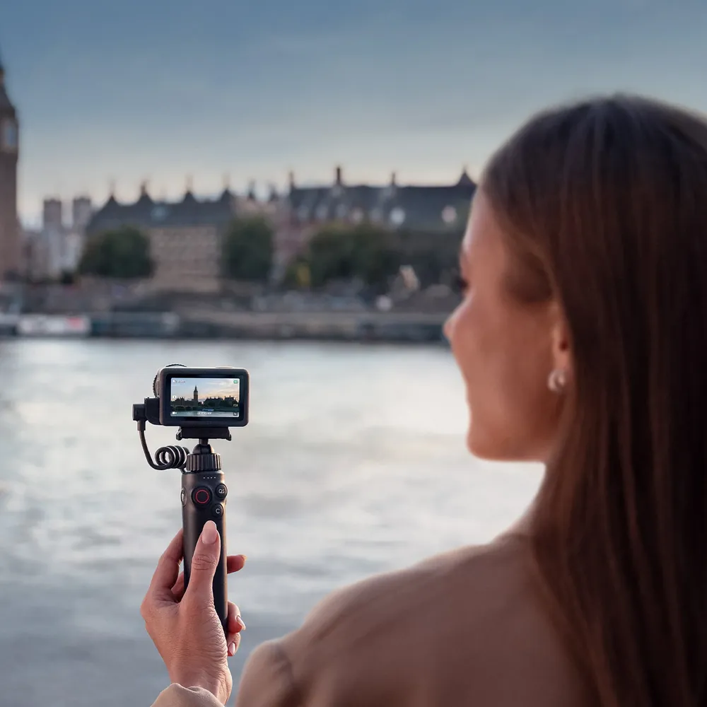 DJI Osmo Action 6 on a handheld grip, filming a riverside city view